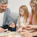 Four family members of different ages engage with toy blocks on a table indoors.